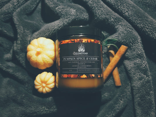 Pumpkin spice candle with decorative pumpkins and cinnamon sticks on a dark fabric background